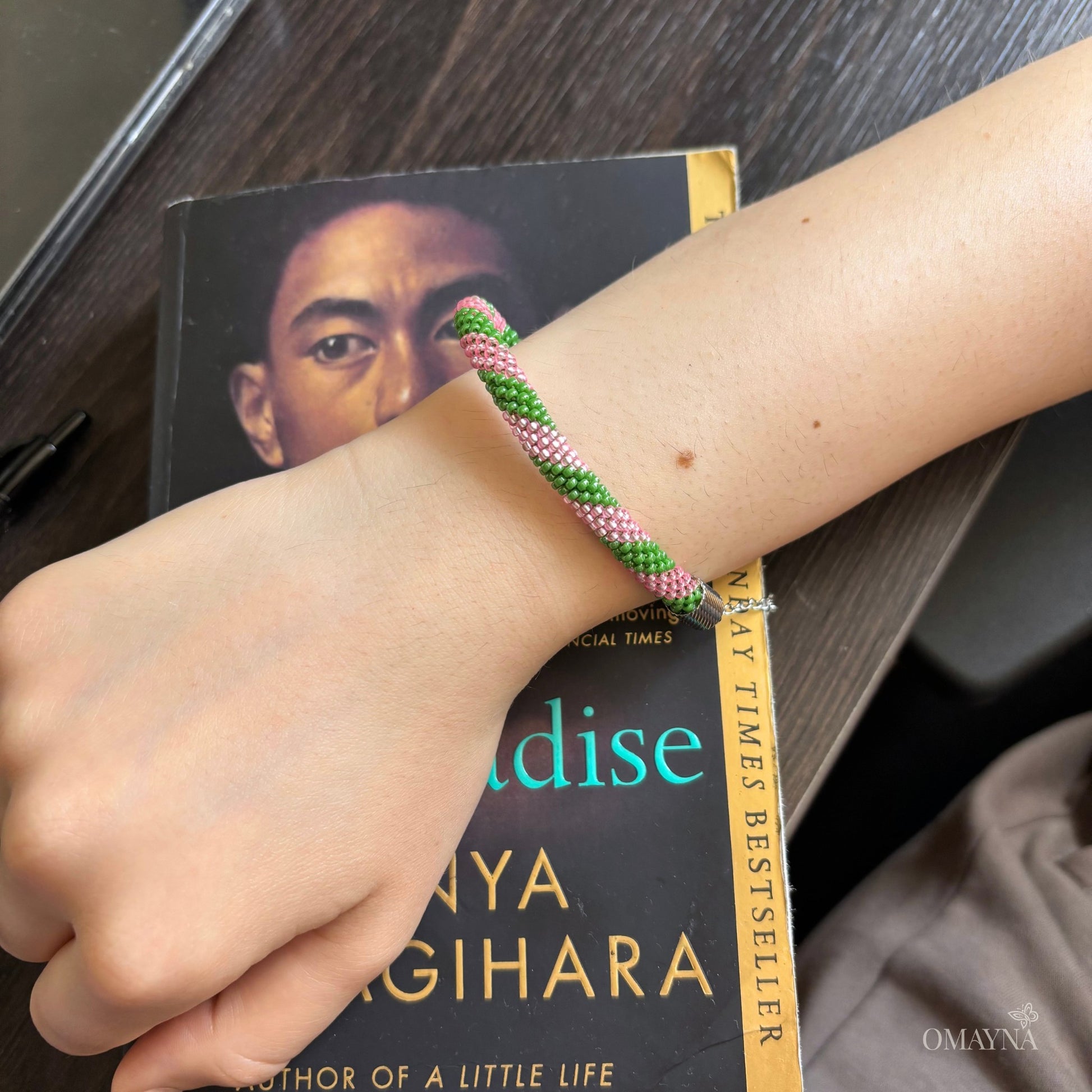 A person wearing a green and pink beaded bracelet on a book 