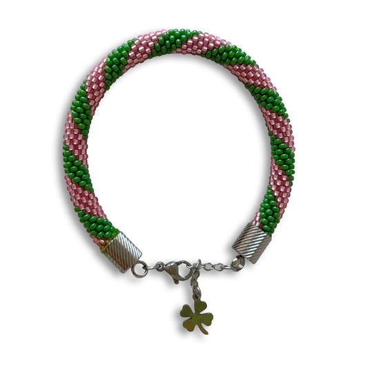 Beaded bracelet in Green and Pink with a clover charm on a white background