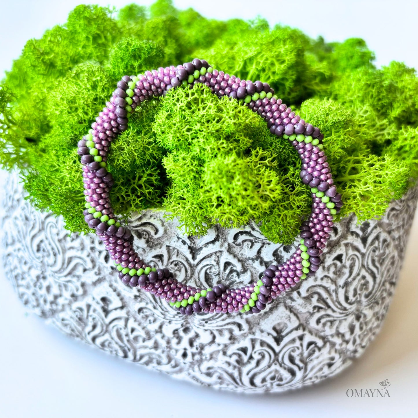 Decorative bracelet with purple and green beads on a textured white surface with green moss.