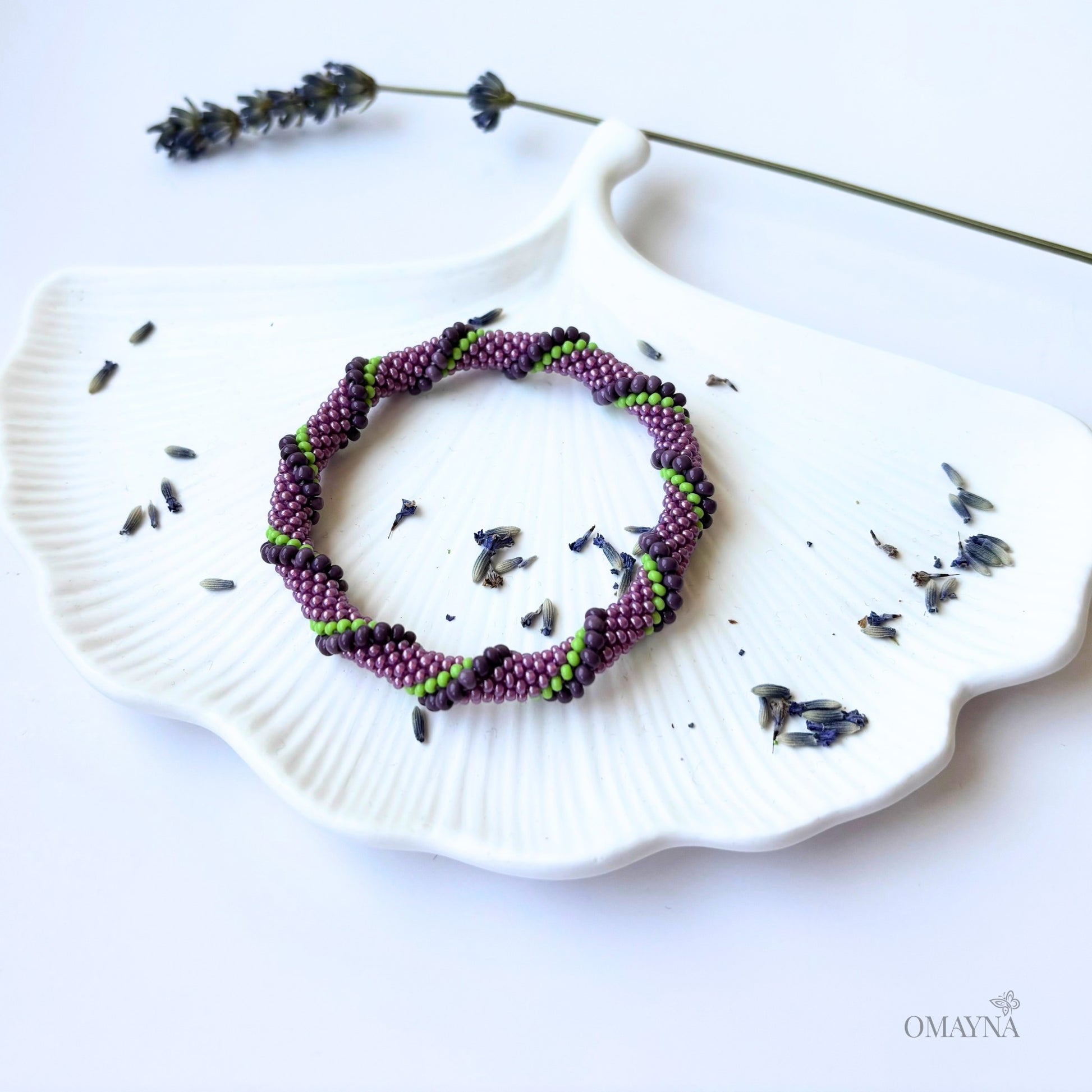Purple and green beaded bracelet on a white jewellery tray with lavender flowers