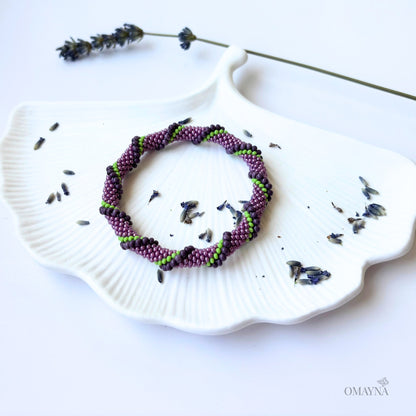 Purple and green beaded bracelet on a white jewellery tray with lavender flowers