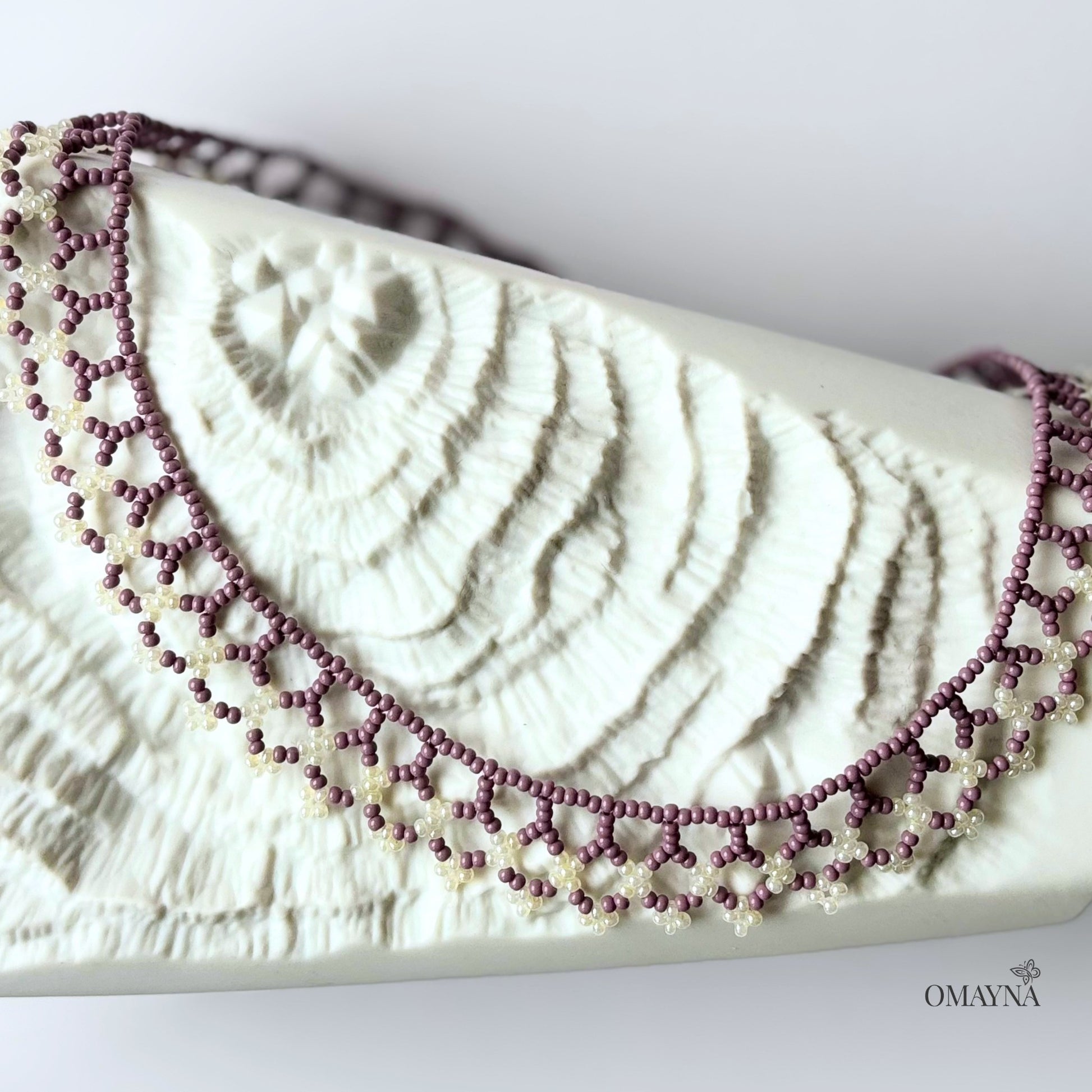 Una beaded necklace in soft purple and cream tones lying on a decorative element