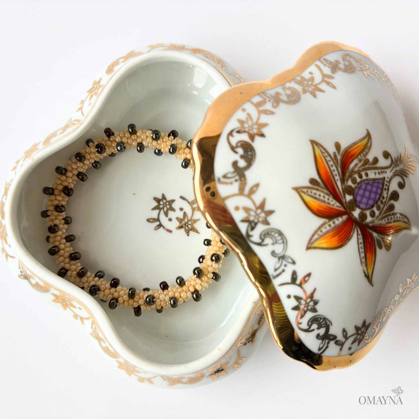 Decorative bone china jewellery box with a brown iris  and pearl beaded bracelet inside on a white background