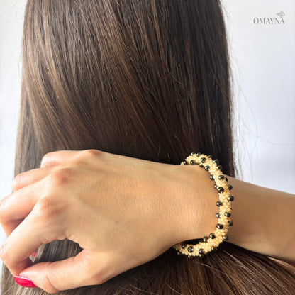 Person wearing a gold and brown beaded bracelet on a plain background