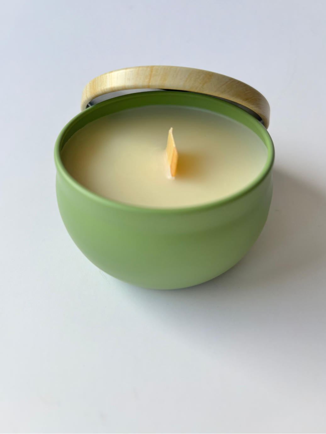 Candle in a green tin with a wooden lid on a white background