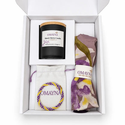 Open Omayna gift box with a Black Cherry scented candle, folded floral scarf and bracelet displayed on a jewellery pouch. Colours purple, yellow and pearl